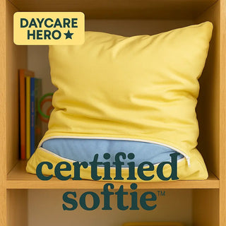 Yellow pillow with blue interior on a wooden shelf, branded as 'Daycare Hero' and 'certified softie'.