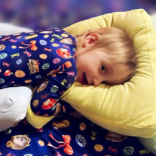 Smiling child cuddling a soft yellow bamboo pillow while lying on a bed in colorful gemstone-patterned pajamas, showing cozy bedtime comfort.