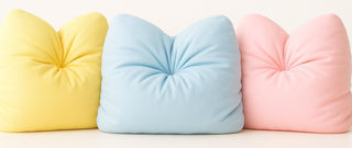 Three bamboo cloud pillows in yellow, blue, and pink on a light background